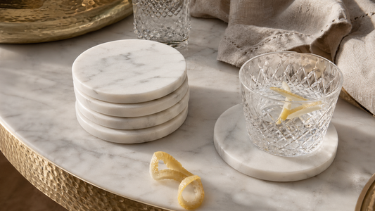 Carrara marble coasters styled with glassware and linen on a TATPUB hosting surface.