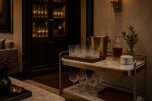 A TATPUB glassware service display with edited glasses, marble coasters, brass ice bucket, teak tray, and storage cabinet nearby.