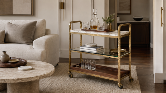 A living room bar cart styled with marble coasters, a teak tray, glassware, and quiet-luxury furniture details.