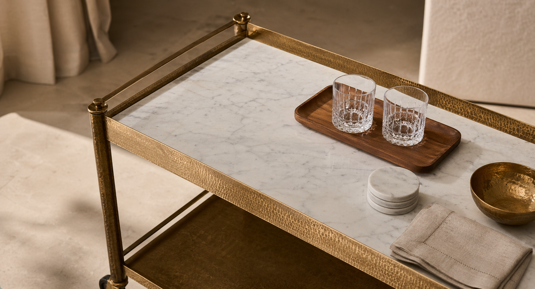 A minimal marble and brass bar cart styled with negative space, marble coasters, glassware, and a teak tray.