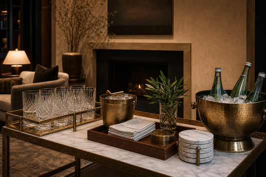 A TATPUB welcome drink station with glassware, brass ice bucket, marble coasters, and teak tray in a warm living room.